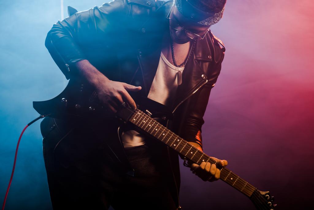 joven rockero masculino en chaqueta de cuero que actúa en la guitarra eléctrica en el escenario con humo e iluminación dramática
  - Foto, imagen