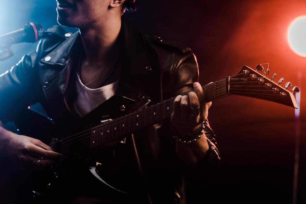 vista parcial del joven cantando en micrófono y tocando la guitarra eléctrica en el escenario durante el concierto de rock
  - Foto, Imagen