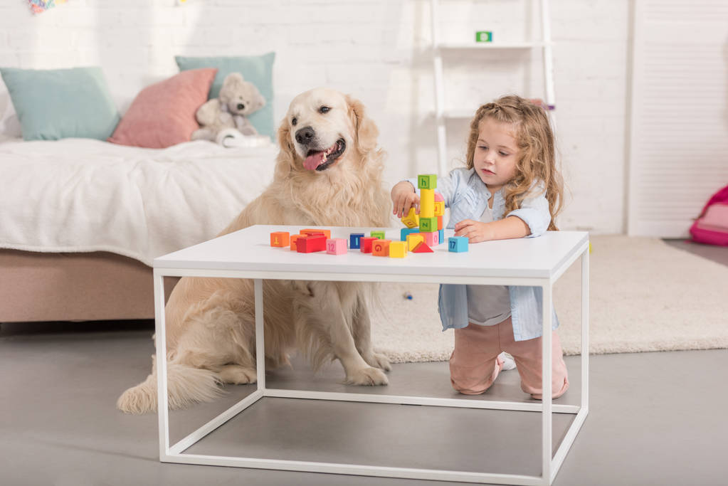 urocze dziecko grając z modułów edukacyjnych, przyjazny pies siedzi w pobliżu stołu w pokoju dzieci - Zdjęcie, obraz