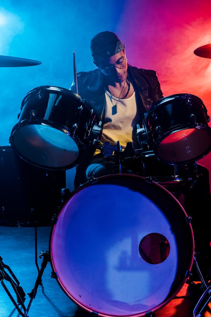 handsome male musician in leather jacket playing drums during rock concert on stage with smoke and dramatic lighting - Photo, Image