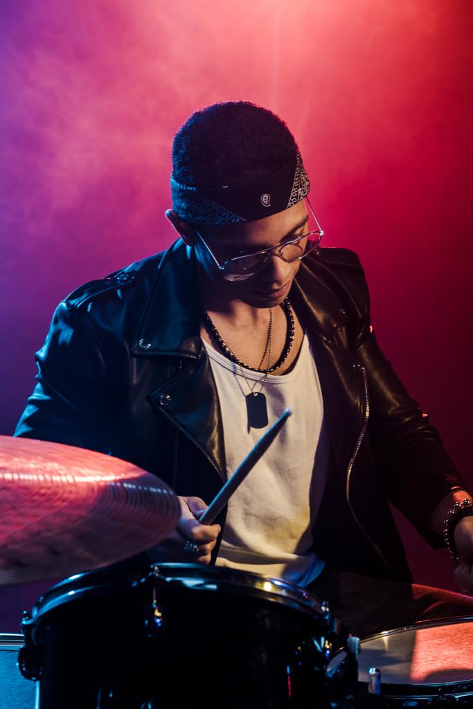 jeune musicien sérieux en veste de cuir jouant de la batterie lors d'un concert de rock sur scène avec de la fumée et un éclairage dramatique
 - Photo, image