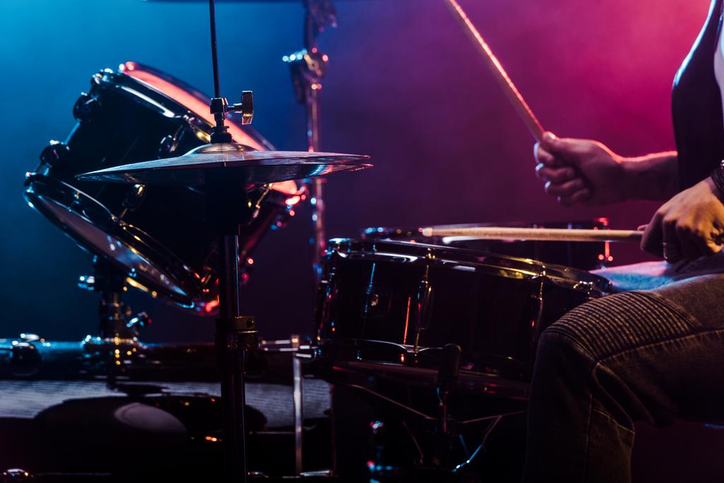 обрезанный кадр мужчины-музыканта, выступающего на барабанах во время рок-концерта на сцене
 - Фото, изображение
