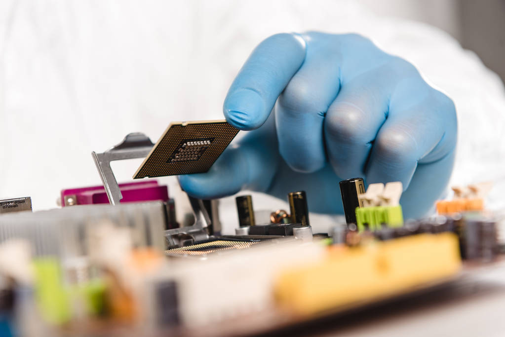 abgeschnittene Ansicht eines Mikrochips in der Hand eines männlichen Wissenschaftlers in der Nähe der Hauptplatine  - Foto, Bild