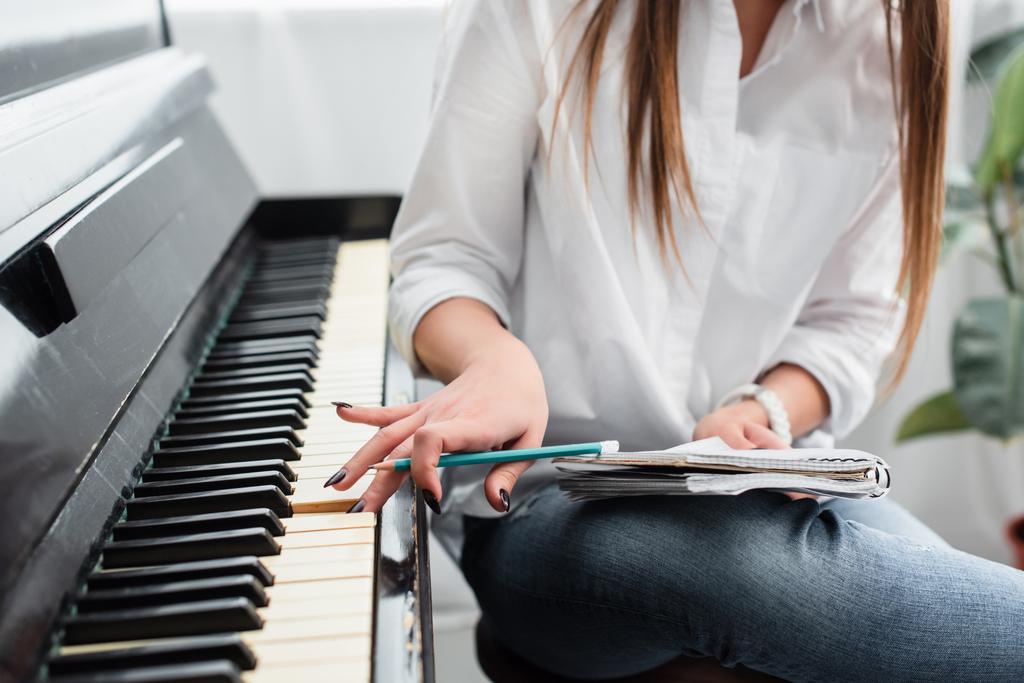 cropped view of girl in white shirt with notebook playing piano and composing music at home - Photo, Image