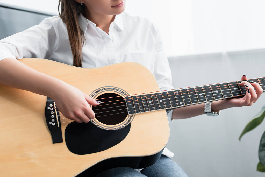 przycięte widzenia dziewczyna siedzi i gra na gitarze w pokoju dziennym - Zdjęcie, obraz