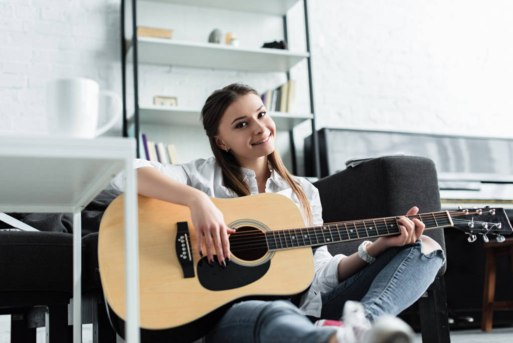 szép mosolygó lány ül, és gitározni nappali - Fotó, kép