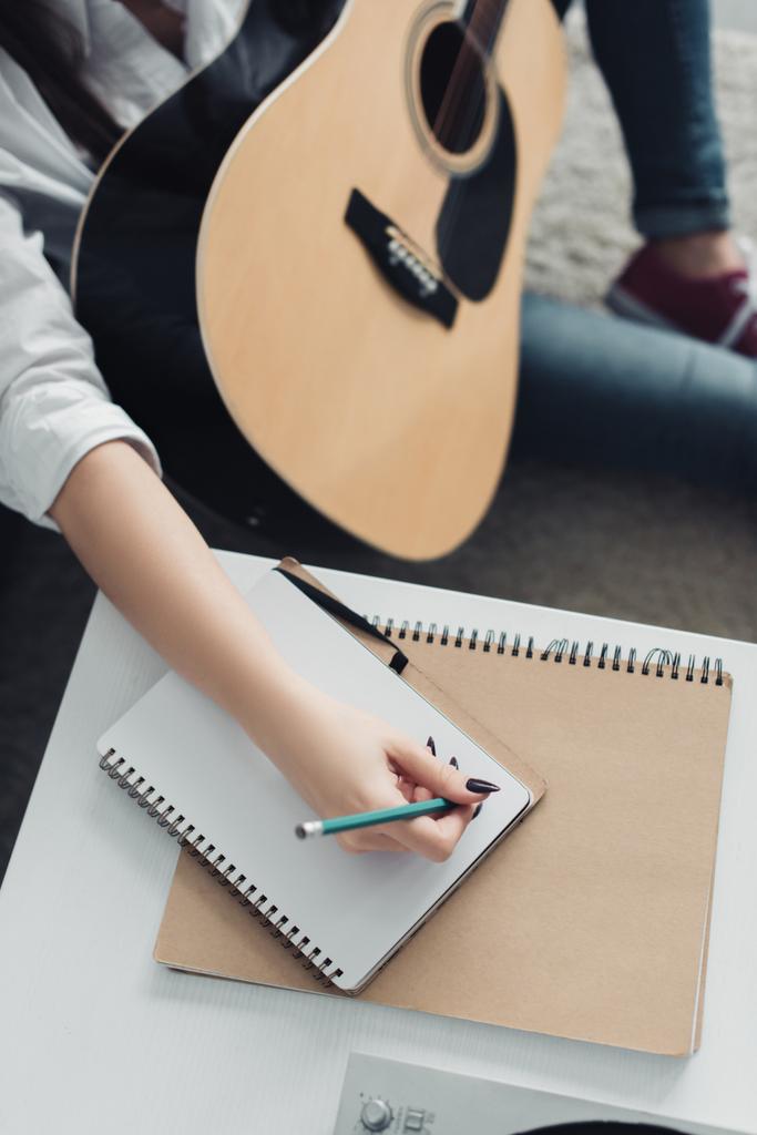 自宅で音楽を作曲しながらノートに書いてアコースティック ギターを持つ少女のトリミング ビュー - 写真・画像