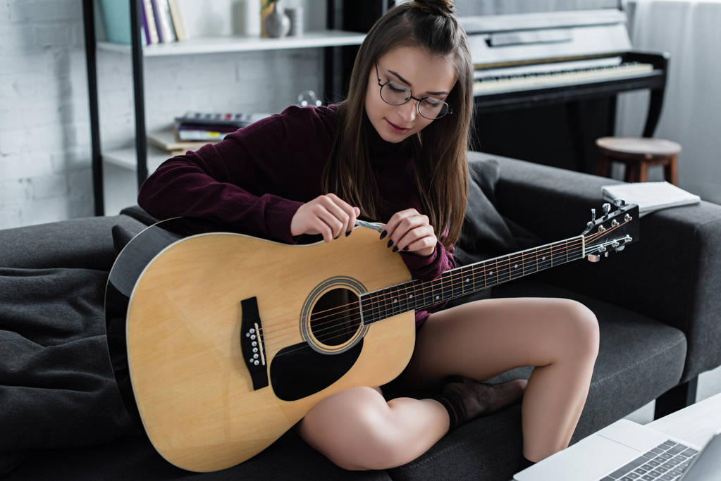 Atrakcyjna dziewczyna siedzi na kanapie z gitara i toczenia marihuany wspólnego w salonie - Zdjęcie, obraz