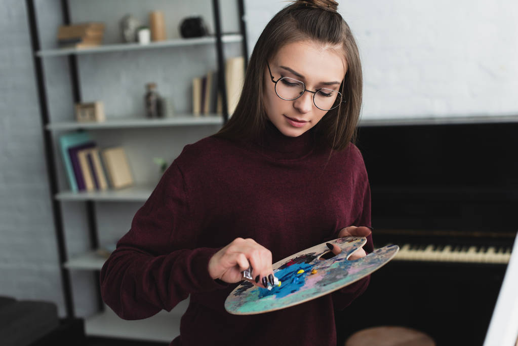 Mädchen im weinroten Pullover mit Palette sitzt und malt zu Hause  - Foto, Bild