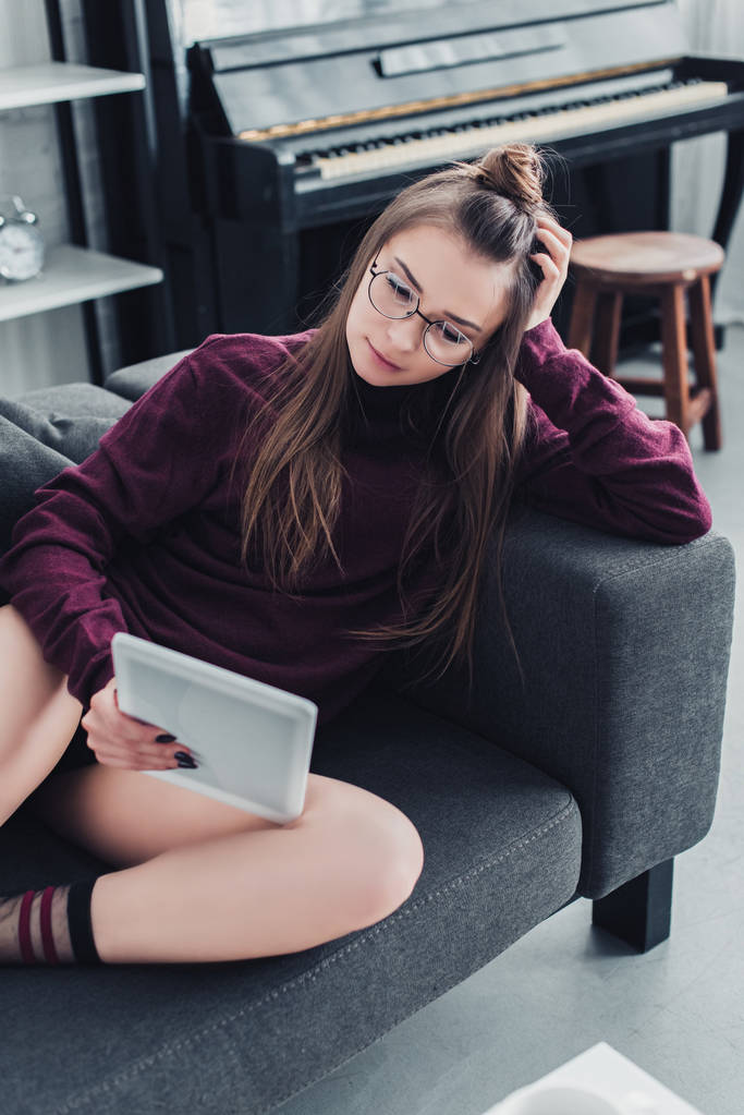 bella ragazza in occhiali sdraiato sul divano e utilizzando tablet digitale in soggiorno
 - Foto, immagini