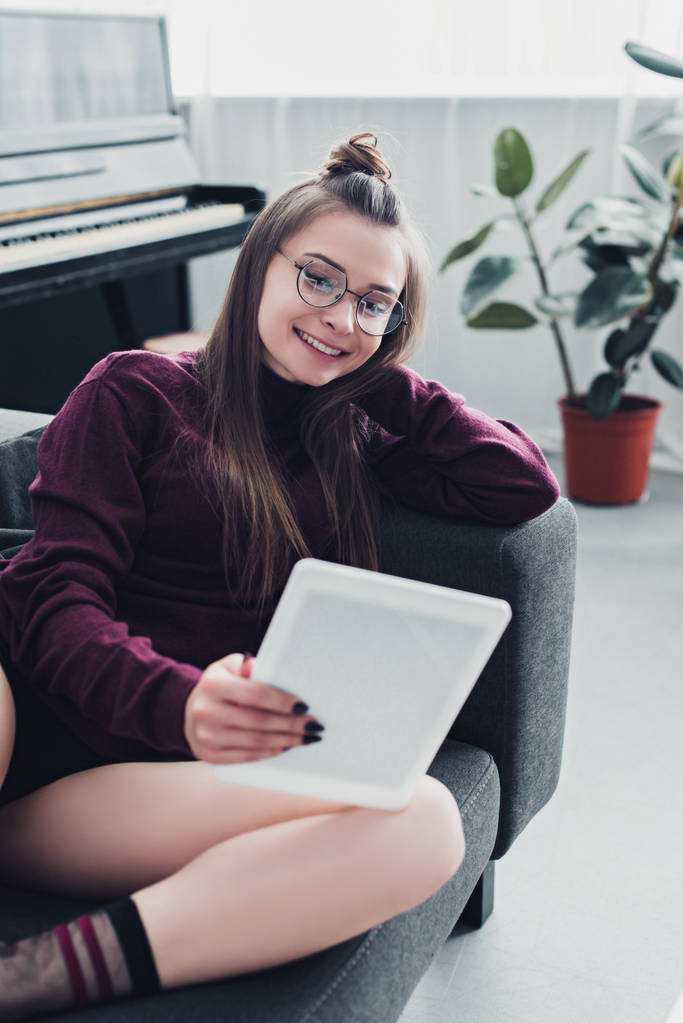 красивая девушка улыбается, лежа на диване и пользуясь цифровым планшетом в гостиной
 - Фото, изображение