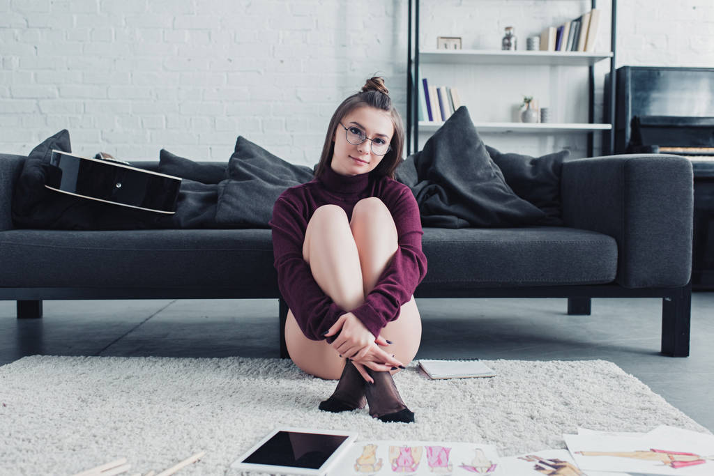 красивий дизайнер сидить на килимі біля дивана і дивиться на камеру у вітальні
 - Фото, зображення