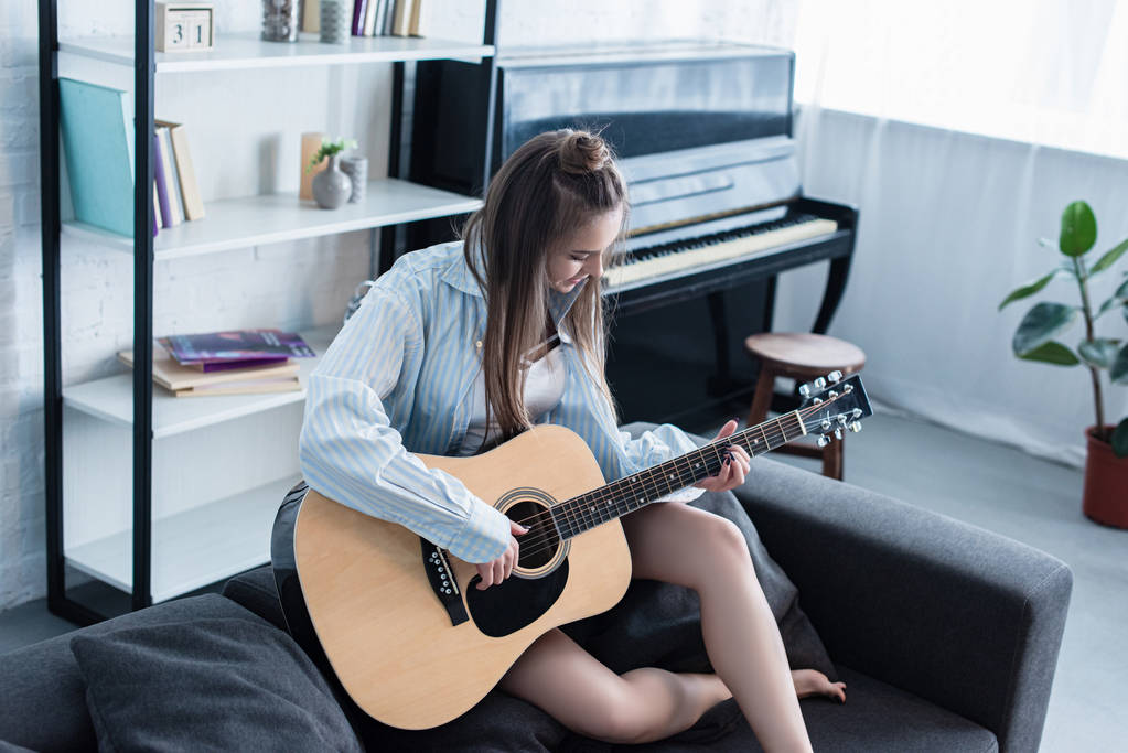kanepede oturan ve oturma odasında akustik gitar çalmak müzisyen - Fotoğraf, Görsel