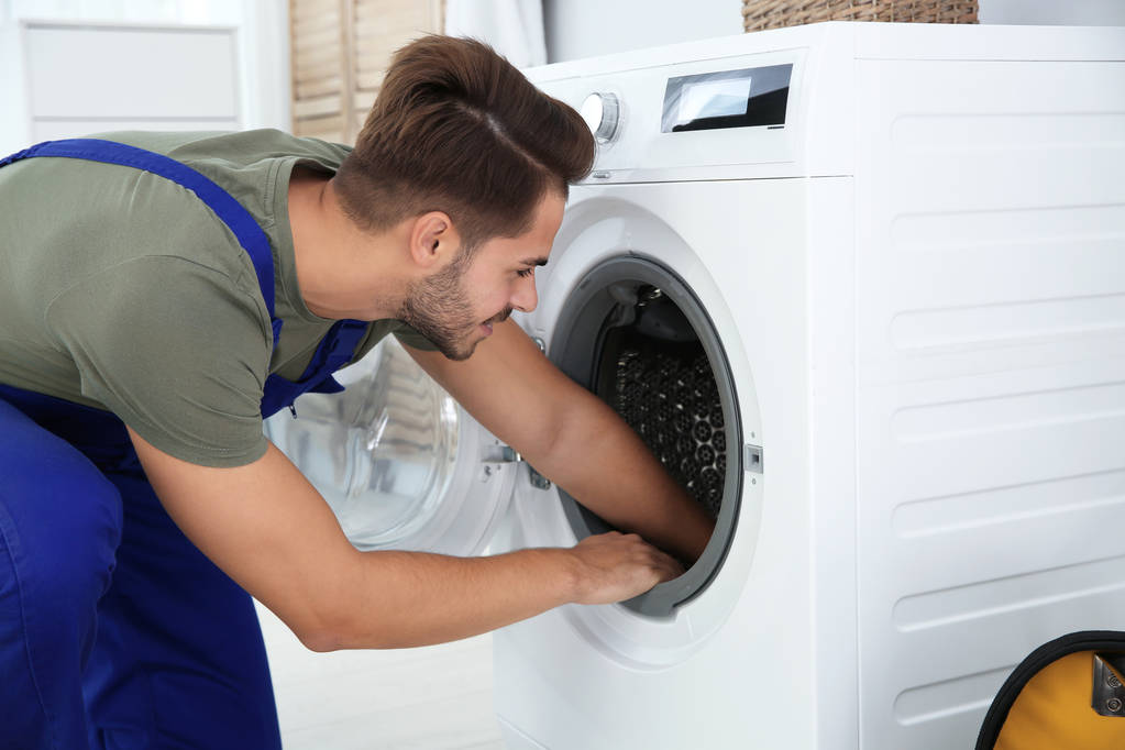 junger Handwerker, der zu Hause eine Waschmaschine repariert. Wäschetag - Foto, Bild