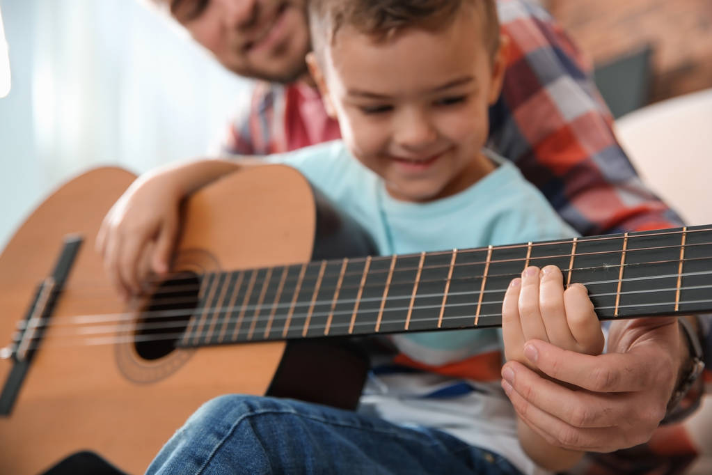Отец учил своего маленького сына играть на гитаре дома
 - Фото, изображение