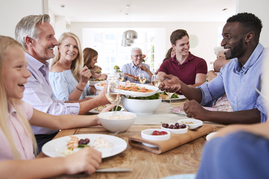Gruppo di famiglia e amici multi-generazione seduti intorno alla tavola e mangiare cibo con bevande
 - Foto, immagini