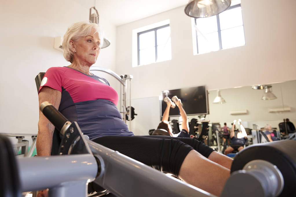 Aktive Seniorin trainiert an Geräten im Fitnessstudio - Foto, Bild