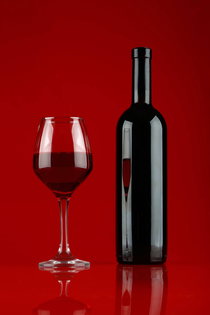Bodegón con una copa y una botella de vino tinto sobre fondo borgoña
 - Foto, Imagen