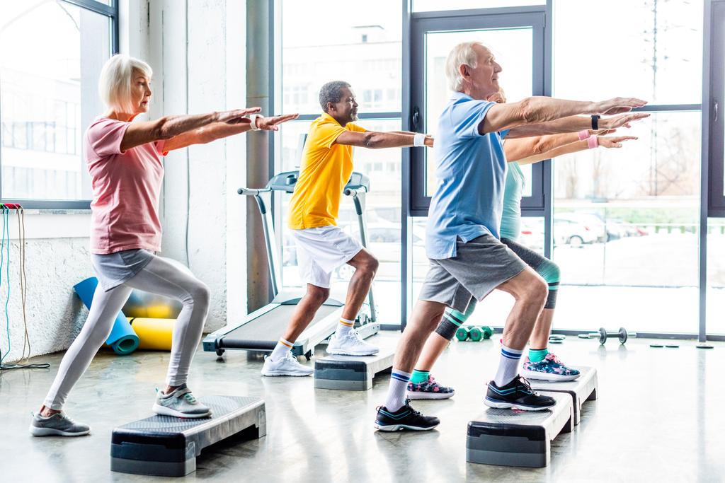 vue de côté des athlètes seniors multiculturels exercice synchrone sur les plates-formes de marche à la salle de gym
 - Photo, image