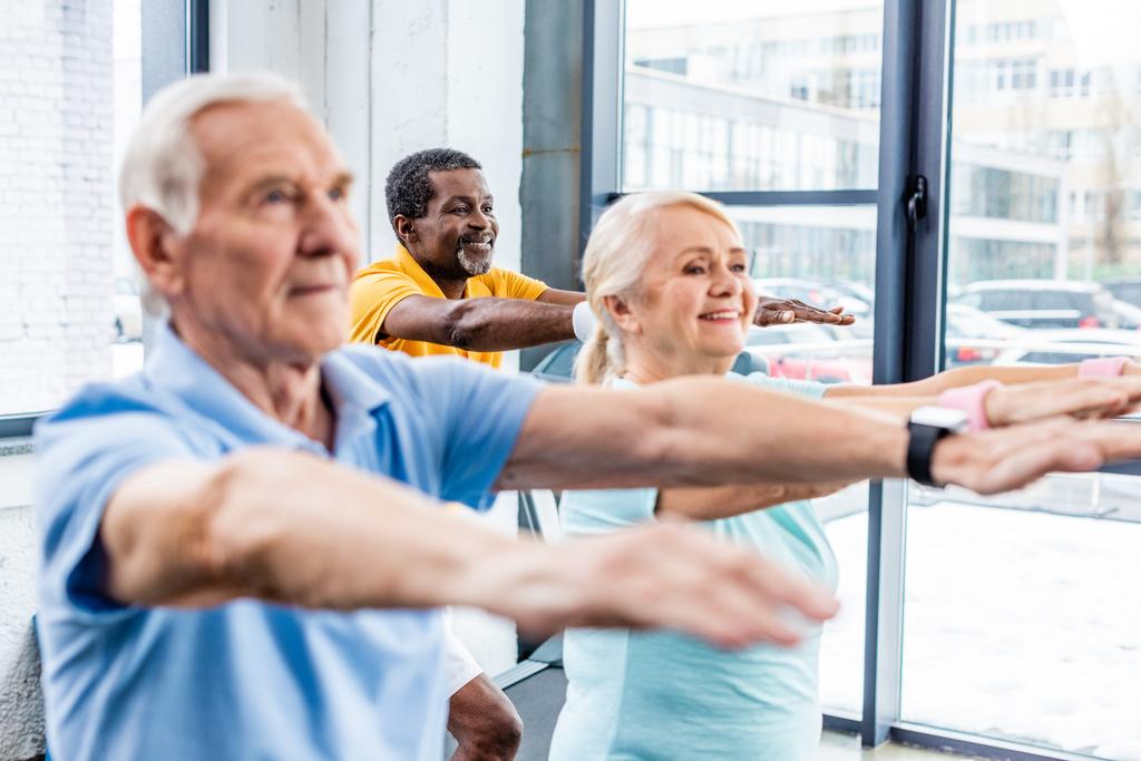 selective focus of multicultural senior athletes synchronous doing exercise at gym - Photo, Image