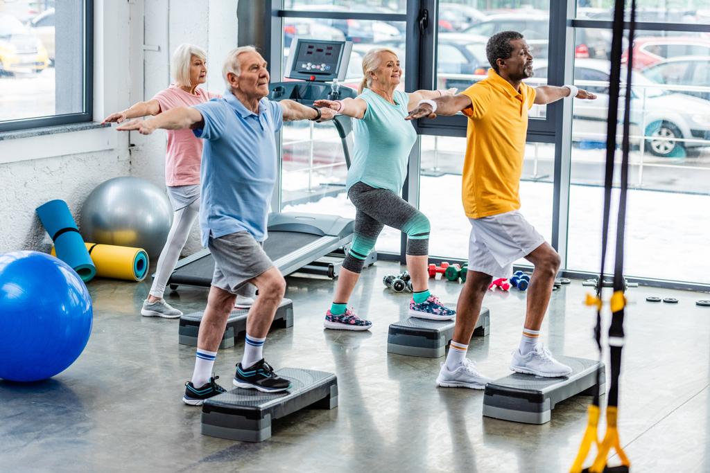 enfoque selectivo de los atletas multiculturales senior ejercicio síncrono en plataformas de paso en el gimnasio
 - Foto, imagen