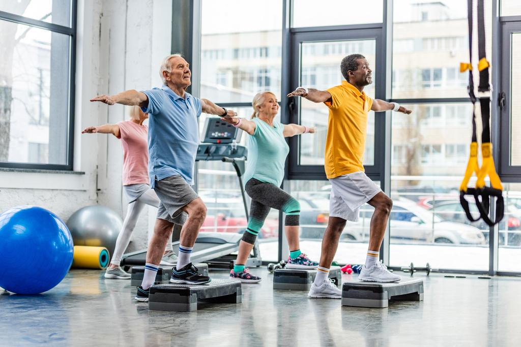 wielokulturowym starszych sportowców synchroniczne, wykonując na platformach krok na siłowni - Zdjęcie, obraz