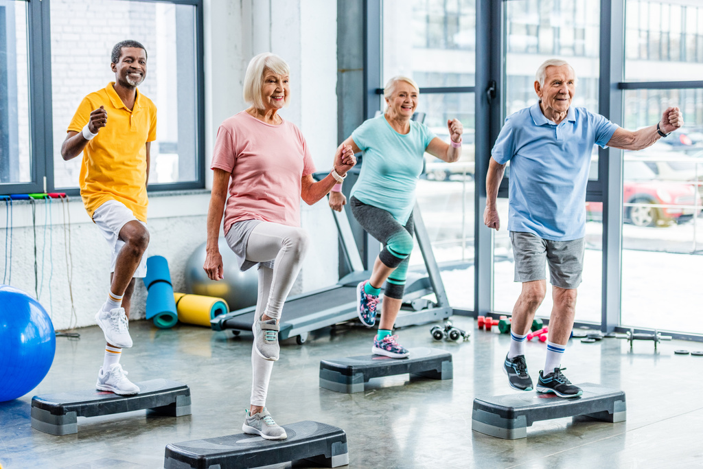lächelnde multiethnische Senioren beim Synchrontraining auf Trittbrettern im Fitnessstudio - Foto, Bild