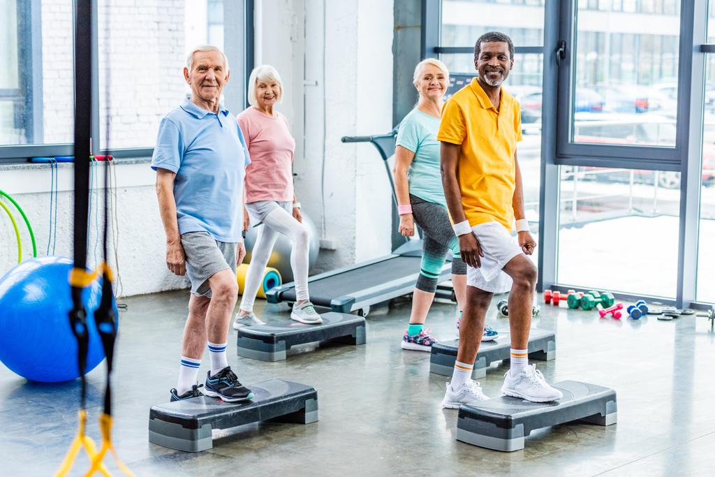 atleti anziani multietnici esercizio sincrono su piattaforme passo in palestra
 - Foto, immagini