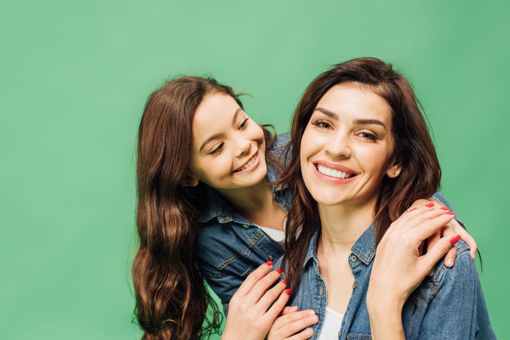 Lächelnde Mutter und Tochter in Jeans umarmen sich vereinzelt auf Grün - Foto, Bild