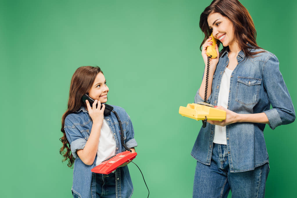 όμορφη μητέρα και κόρη μιλώντας σε vintage τηλέφωνα που απομονώνονται σε πράσινο - Φωτογραφία, εικόνα
