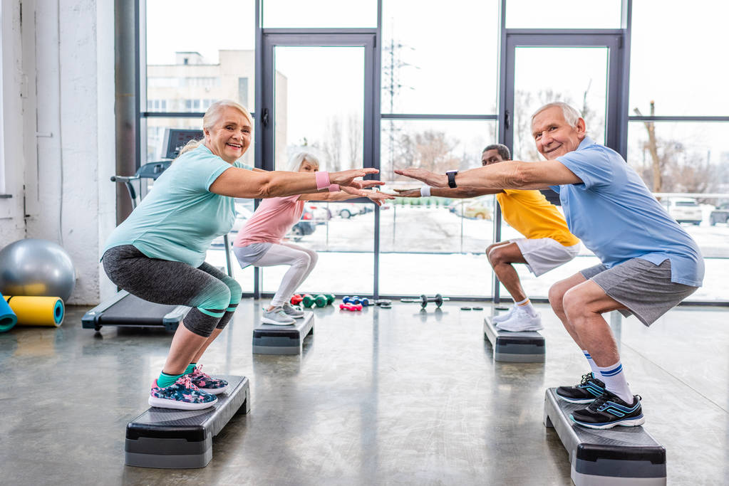 felice anziani sportivi multietnici sincrono facendo squat su piattaforme passo in palestra
 - Foto, immagini
