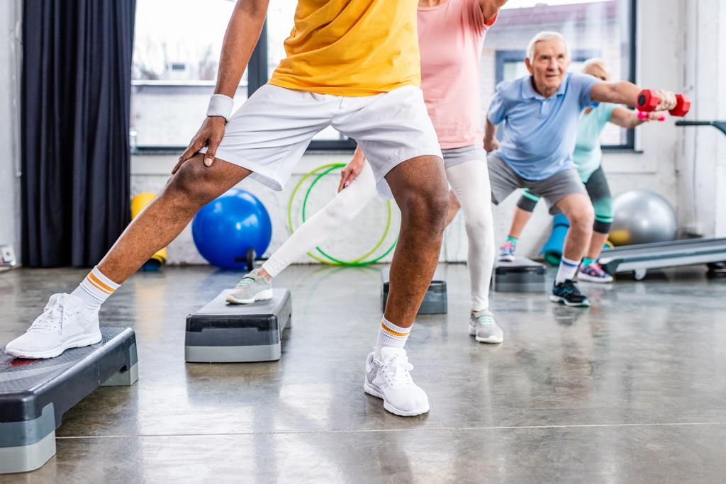 tiro recortado de atletas seniores exercício síncrono com halteres em plataformas de passo no ginásio
 - Foto, Imagem