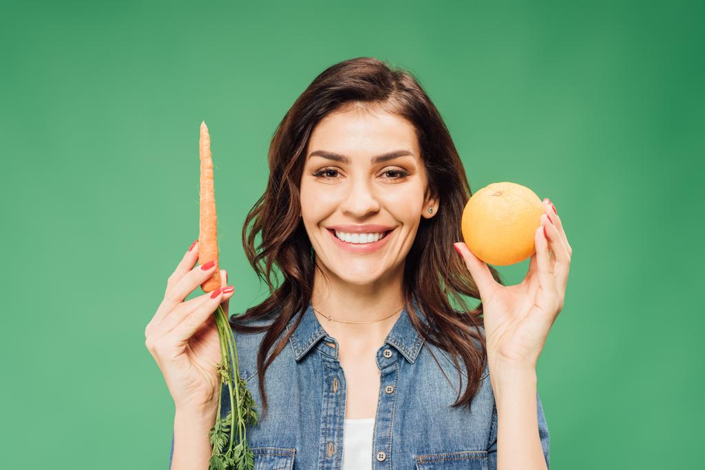 femme souriante en denim tenant orange et carotte isolée sur vert
 - Photo, image