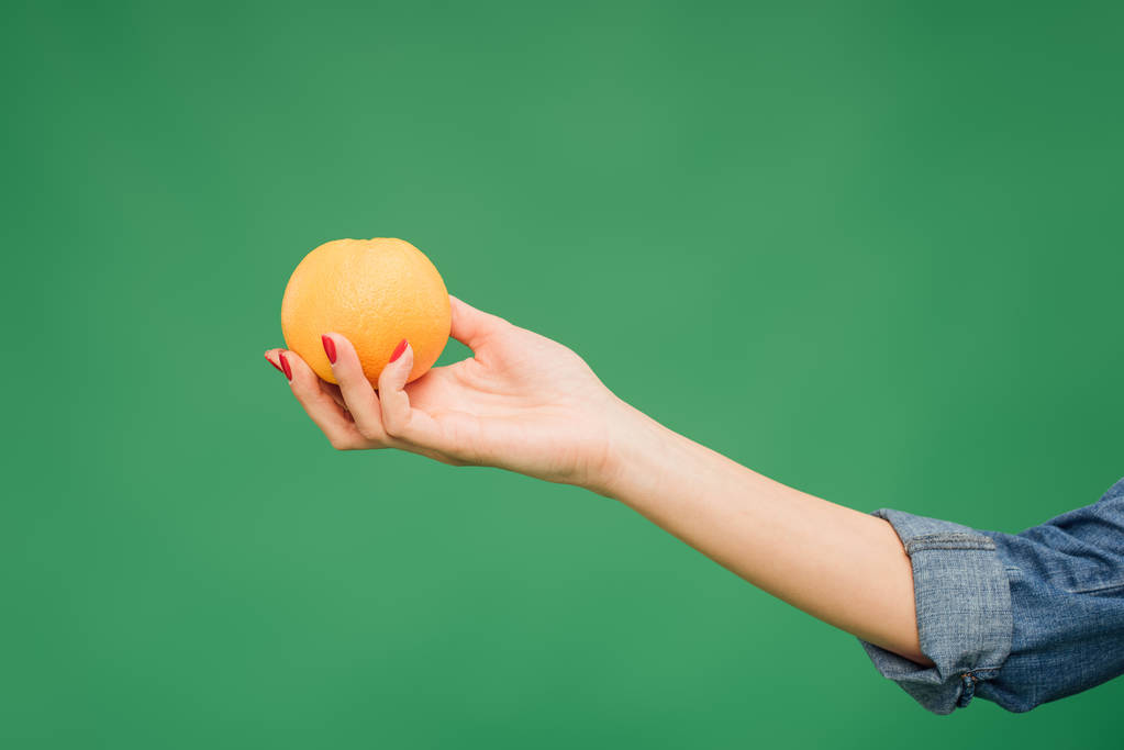 oříznutý pohled ženy držící oranžové v ruce izolované na zelené - Fotografie, Obrázek