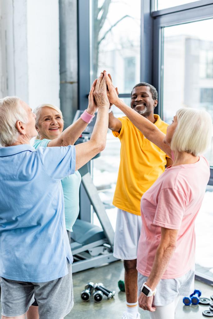 Sportifs multiculturels seniors souriants mettant la main ensemble à la salle de gym
 - Photo, image