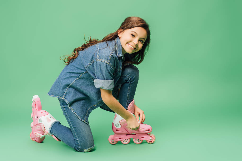 cute child putting on rollerblades and looking at camera on green background - Photo, Image