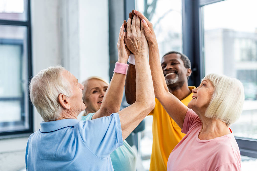 вибірковий фокус щасливих старших мультикультурних спортсменів, що складають руки в спортзалі
 - Фото, зображення