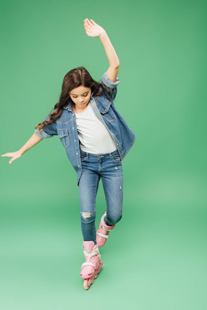kind in denim skaten met uitgestrekte handen op groene achtergrond - Foto, afbeelding