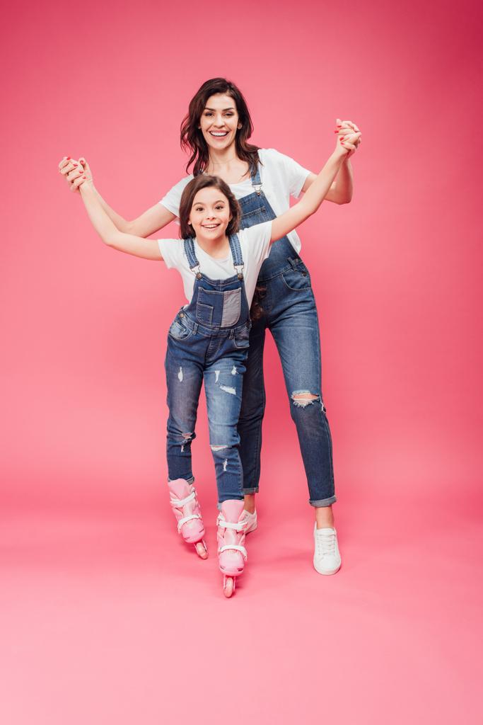 beautiful mother teaching daughter rollerblading on pink background - Photo, Image