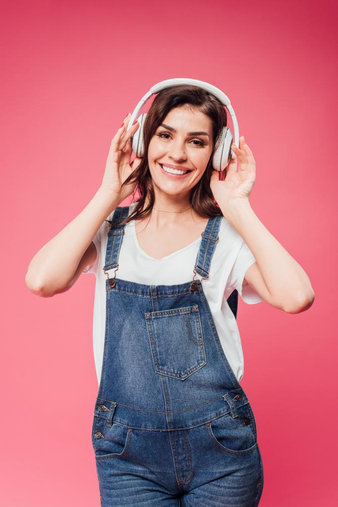 усміхнена жінка слухає музику в навушниках ізольовано на рожевому
 - Фото, зображення