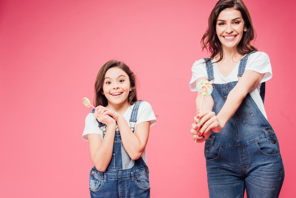 happy mother and daughter holding lollipops and looking at camera isolated on pink - Photo, Image