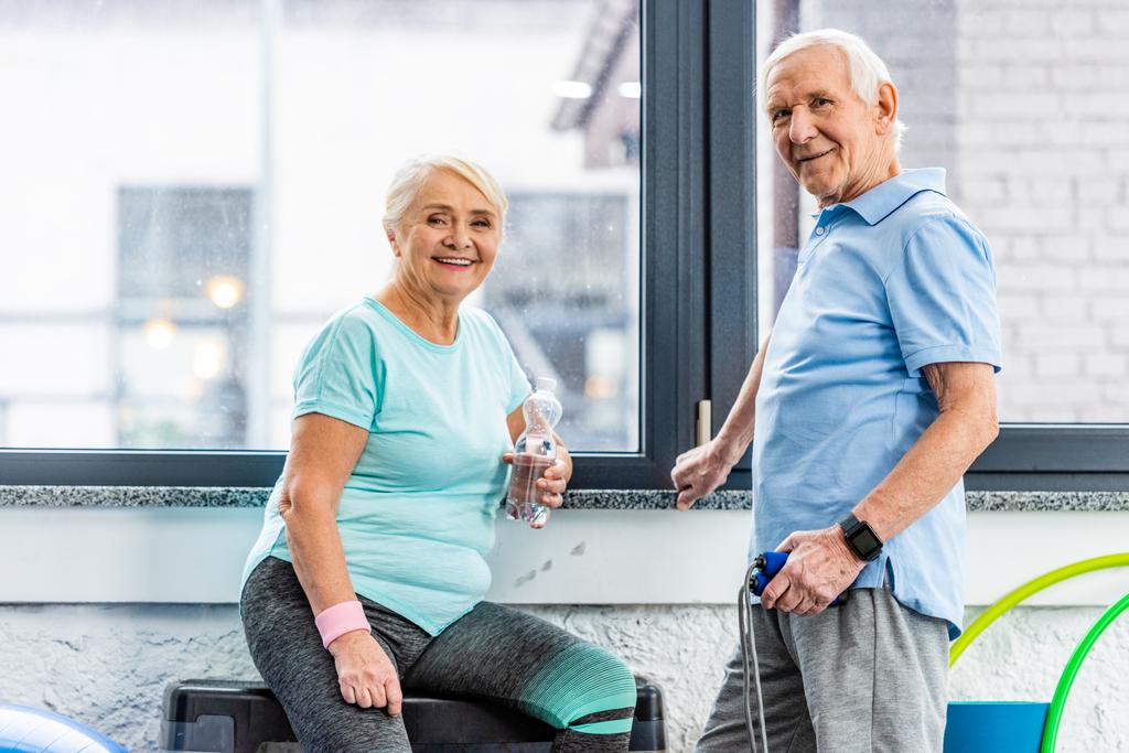 Seniorenpaar mit Springseil und Wasserflasche rastet in Sporthalle aus - Foto, Bild