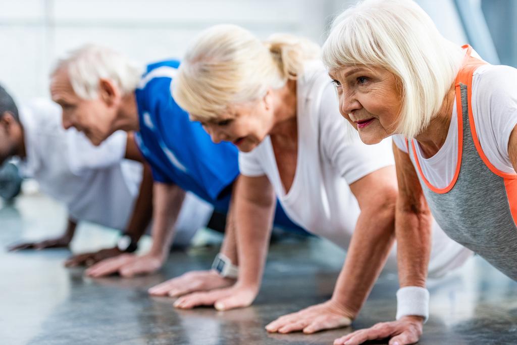 Selektiver Fokus der Senior-Sportlerin und ihrer Freunde beim Planken im Fitnessstudio - Foto, Bild