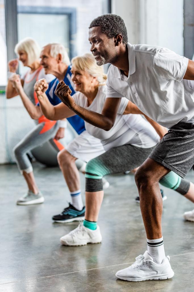african american sportsman synchronous exercising with friends at sports hall - Photo, Image