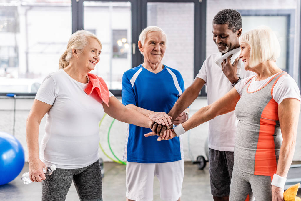 усміхнені старші багатогранні друзі складають руки в спортивному залі
  - Фото, зображення