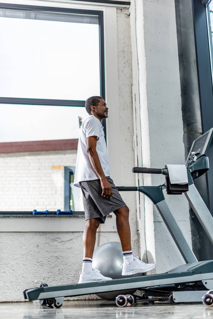 χαμηλή γωνία προβολής της μέσης ηλικίας αφρικανική αμερικανική άνθρωπος άσκηση σε διάδρομο στο γυμναστήριο - Φωτογραφία, εικόνα