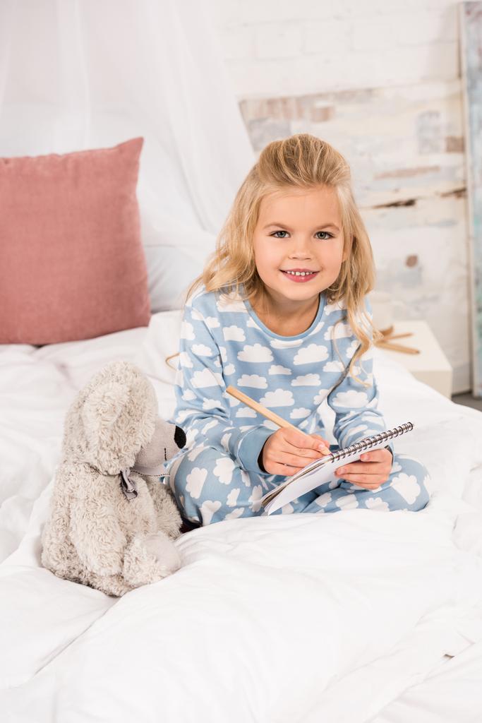 adorable enfant assis au lit et écrivant dans un cahier
 - Photo, image