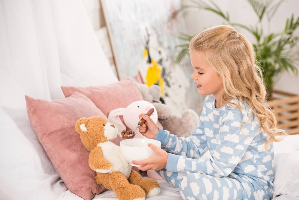 adorabile bambino in pigiama che alimenta giocattoli morbidi a letto
 - Foto, immagini