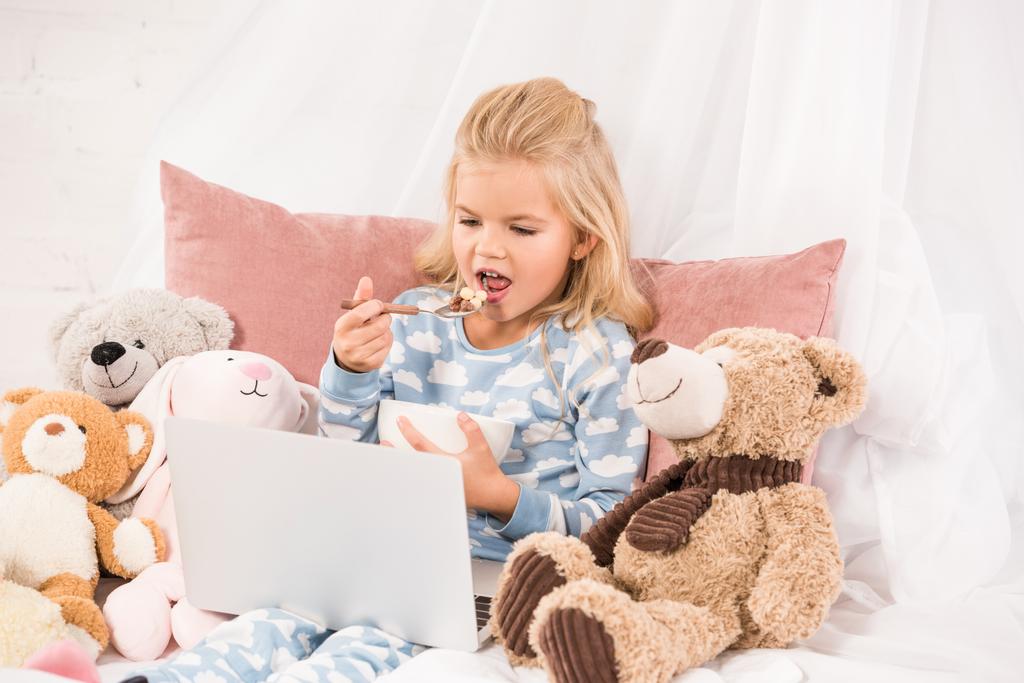 aranyos gyerek eszik kukoricapehely és néz rajzfilmeket az ágyban - Fotó, kép