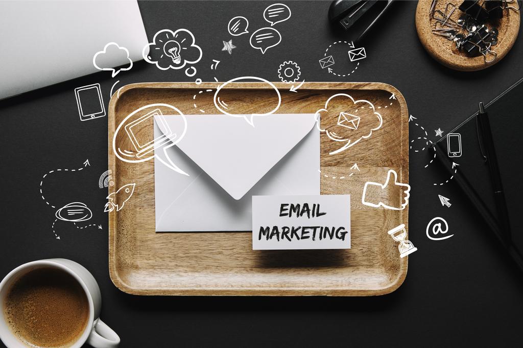 flache Liege mit Holztablett mit Umschlag und Visitenkarte mit "E-Mail Marketing" Schriftzug auf schwarzem Hintergrund mit Laptop und Schreibwaren - Foto, Bild